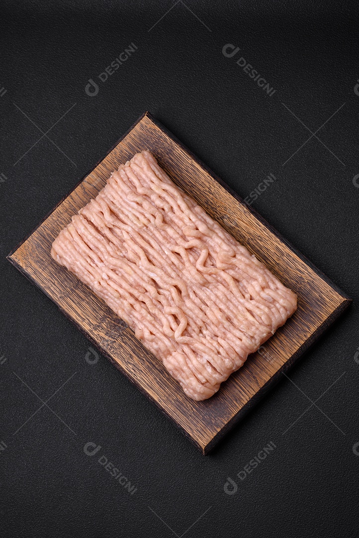 Frango picado fresco com sal, especiarias e ervas em uma tábua de madeira sobre um fundo escuro de concreto