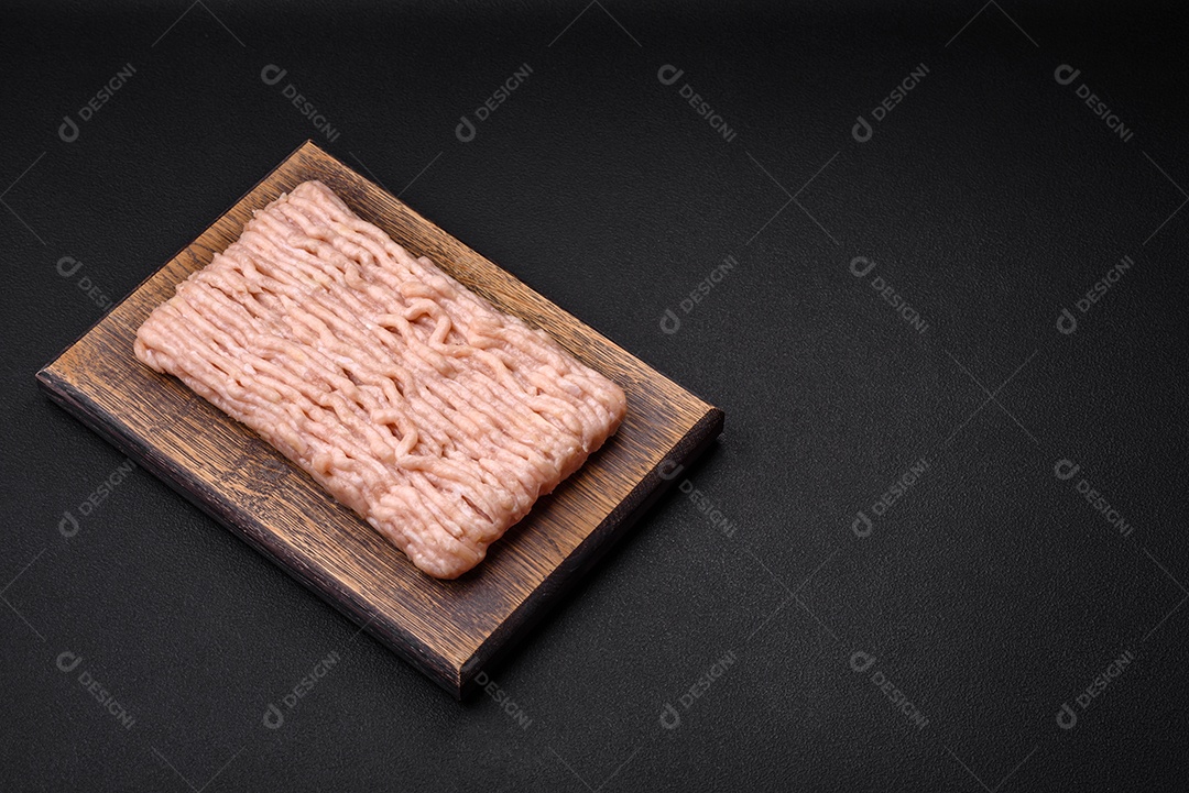 Frango picado fresco com sal, especiarias e ervas em uma tábua de madeira sobre um fundo escuro de concreto