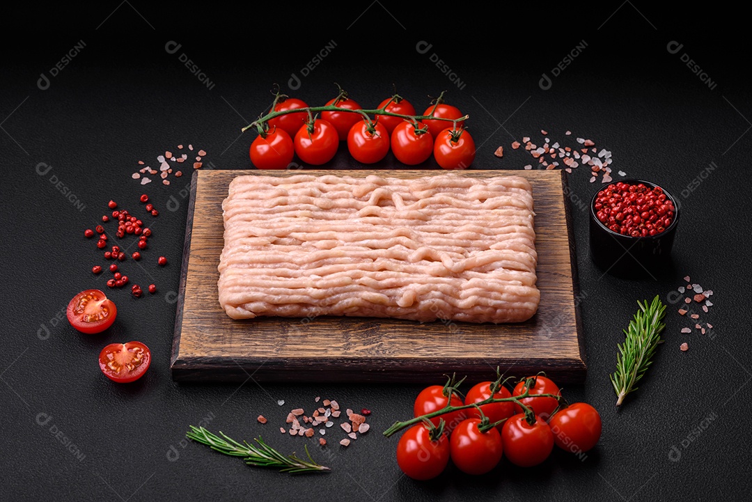 Frango picado fresco com sal, especiarias e ervas em uma tábua de madeira sobre um fundo escuro de concreto