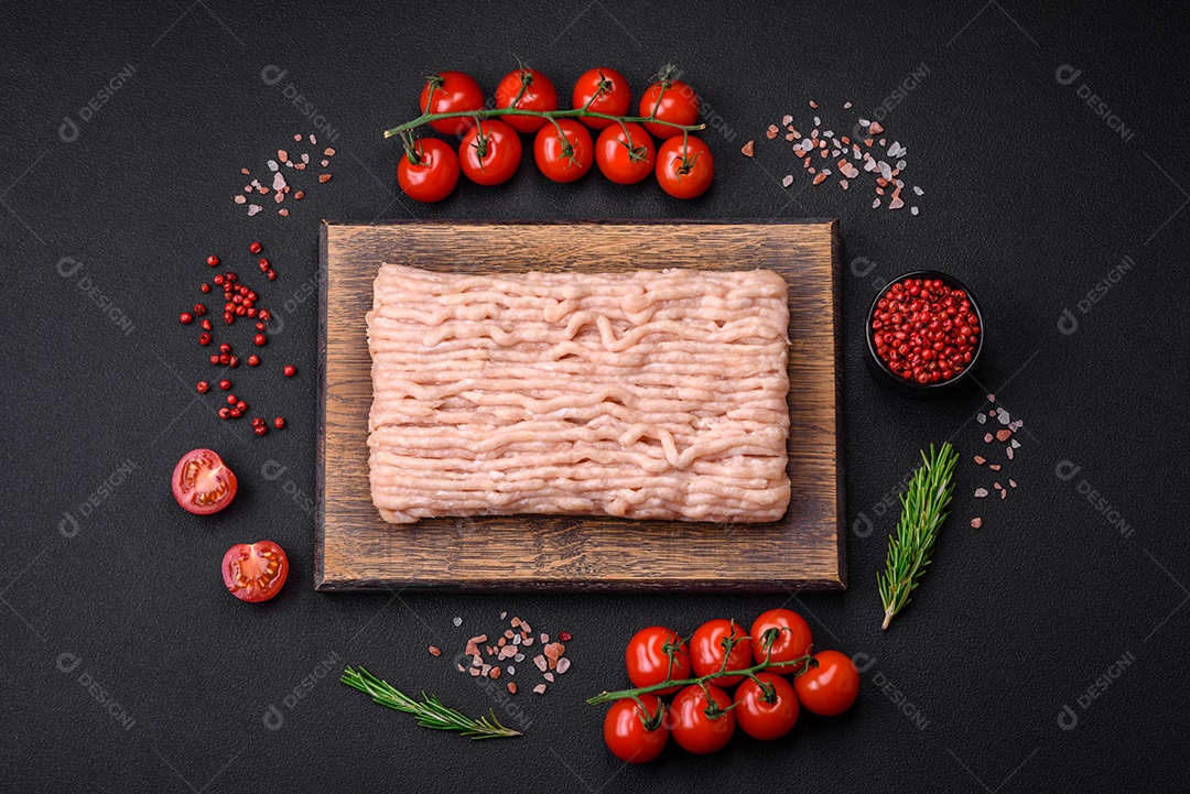 Frango picado fresco com sal, especiarias e ervas em uma tábua de madeira sobre um fundo escuro de concreto