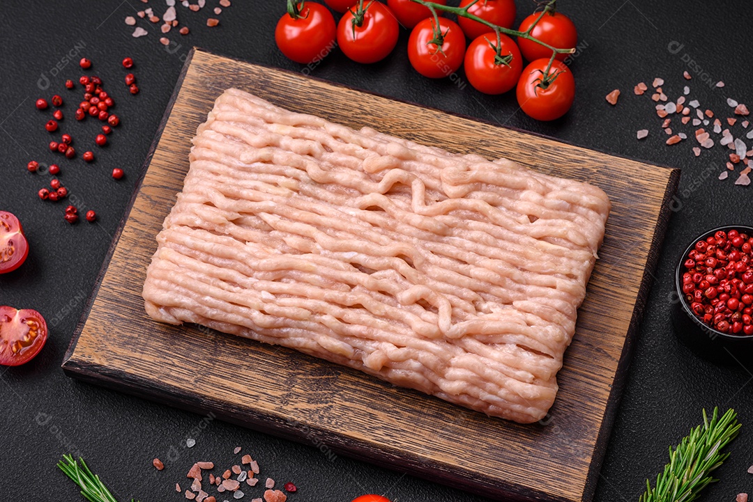 Frango picado fresco com sal, especiarias e ervas em uma tábua de madeira sobre um fundo escuro de concreto