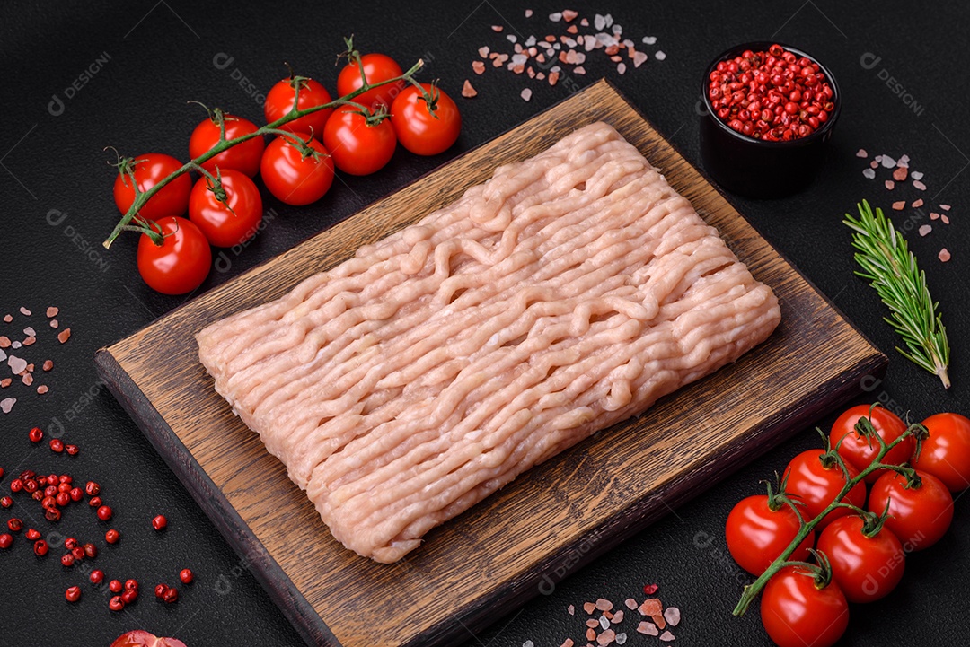 Frango picado fresco com sal, especiarias e ervas em uma tábua de madeira sobre um fundo escuro de concreto