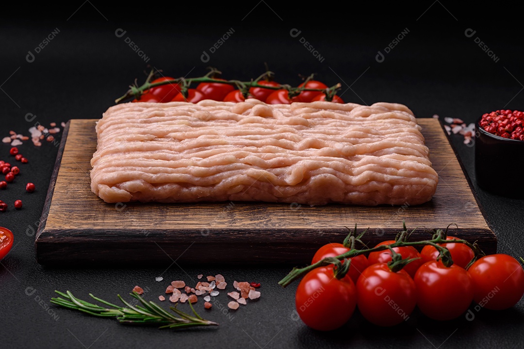 Frango picado fresco com sal, especiarias e ervas em uma tábua de madeira sobre um fundo escuro de concreto