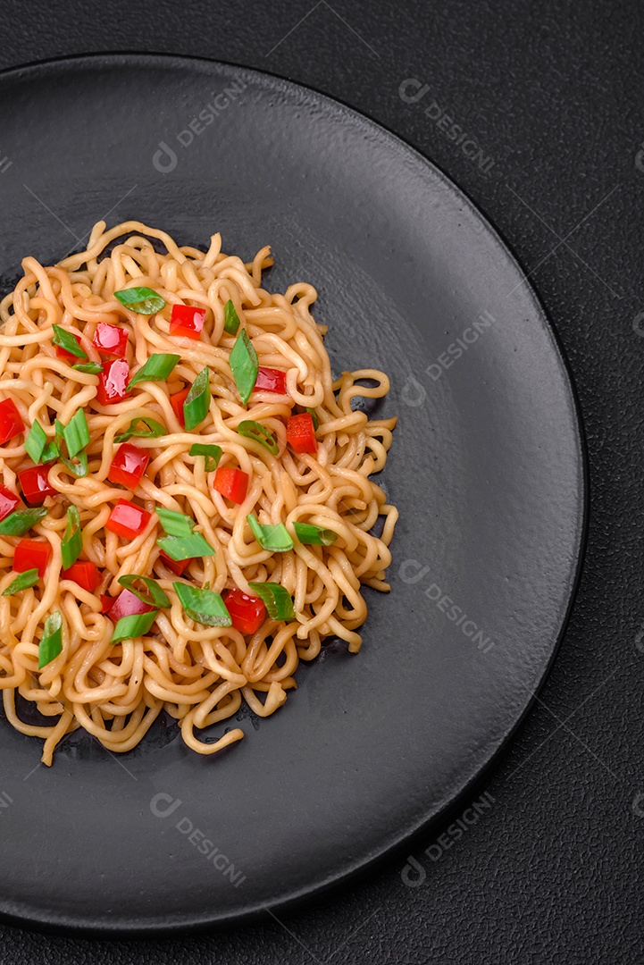 Delicioso macarrão asiático fresco com legumes, sal, especiarias e ervas em uma placa cerâmica sobre um fundo escuro de concreto