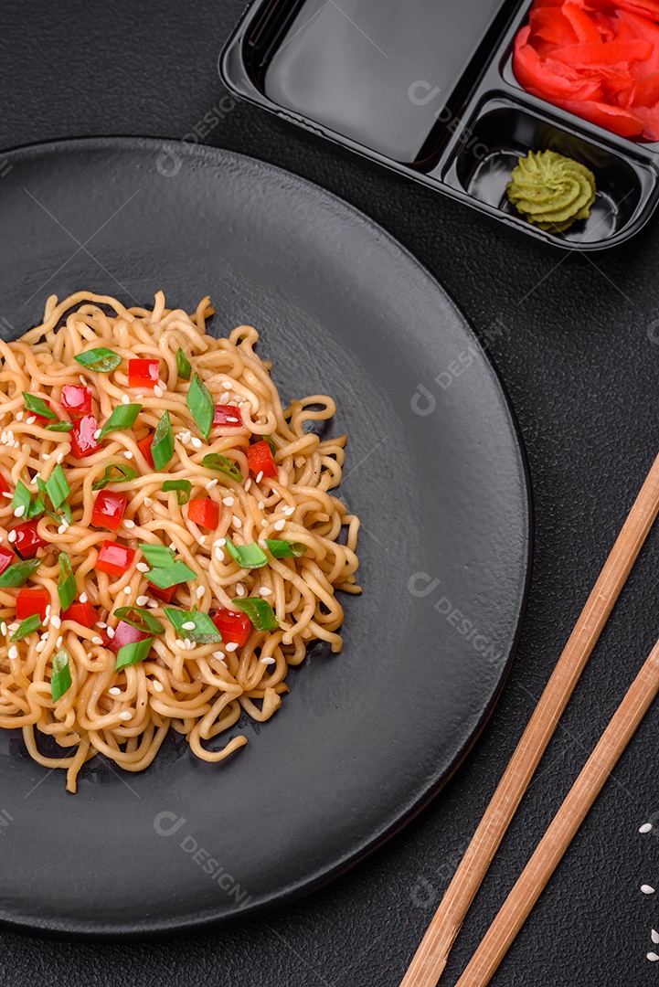 Delicioso macarrão asiático fresco com legumes, sal, especiarias e ervas em uma placa cerâmica sobre um fundo escuro de concreto