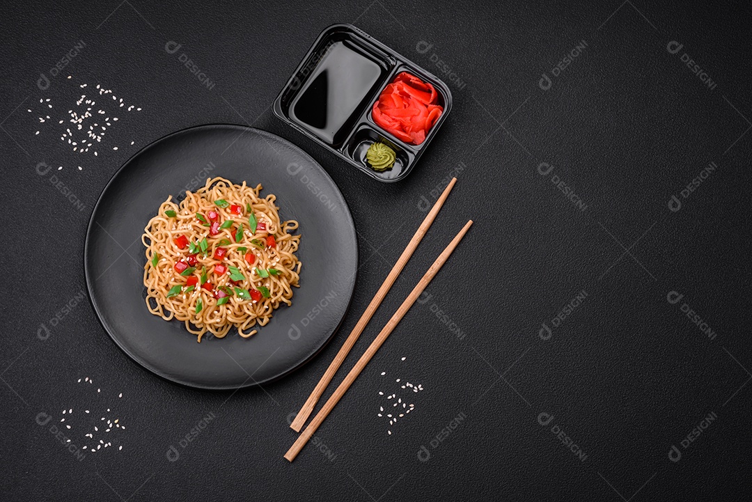 Delicioso macarrão asiático fresco com legumes, sal, especiarias e ervas em uma placa cerâmica sobre um fundo escuro de concreto