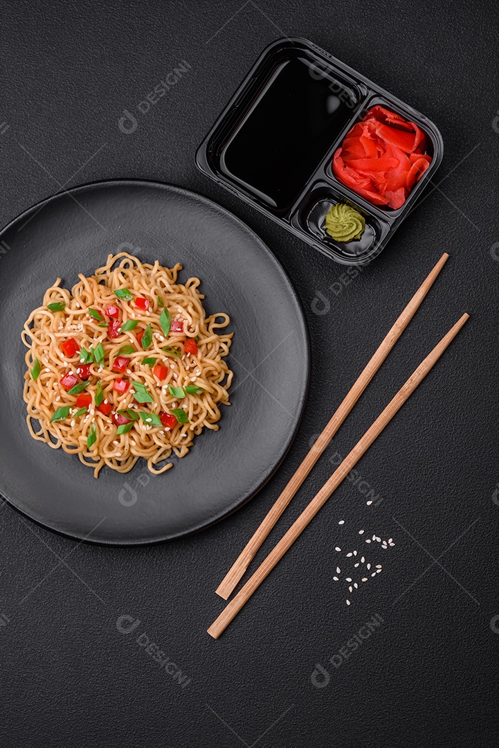 Delicioso macarrão asiático fresco com legumes, sal, especiarias e ervas em uma placa cerâmica sobre um fundo escuro de concreto