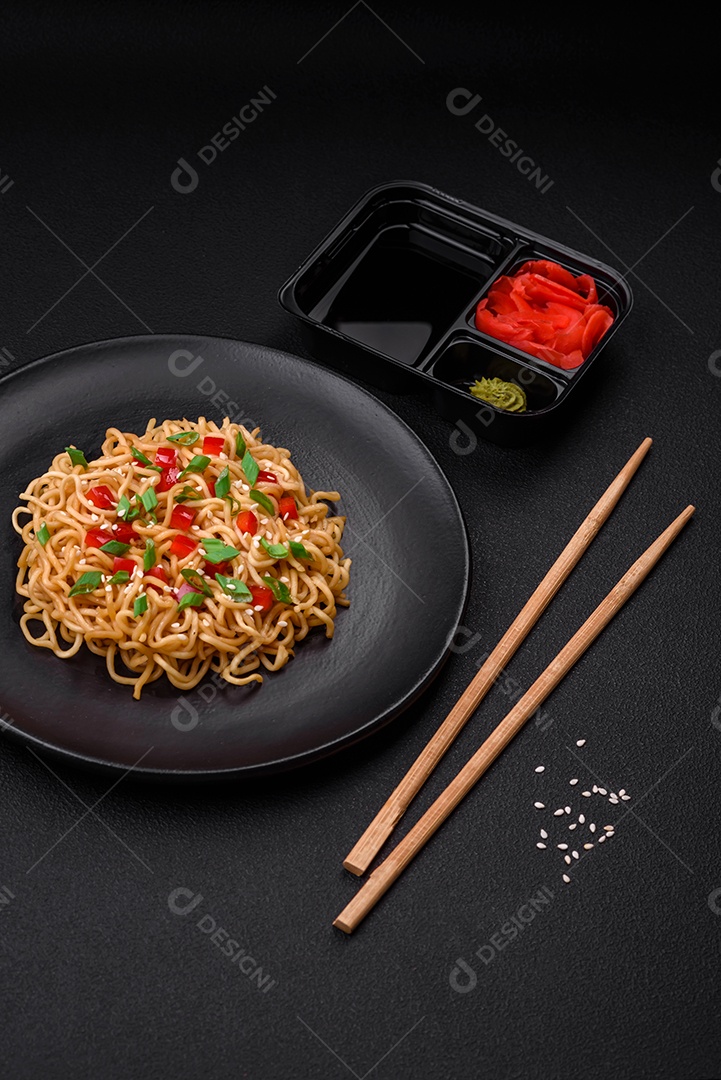 Delicioso macarrão asiático fresco com legumes, sal, especiarias e ervas em uma placa cerâmica sobre um fundo escuro de concreto