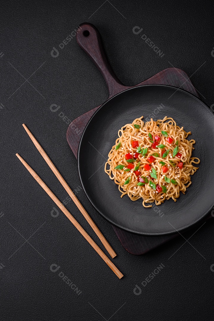 Delicioso macarrão asiático fresco com legumes, sal, especiarias e ervas em uma placa cerâmica sobre um fundo escuro de concreto