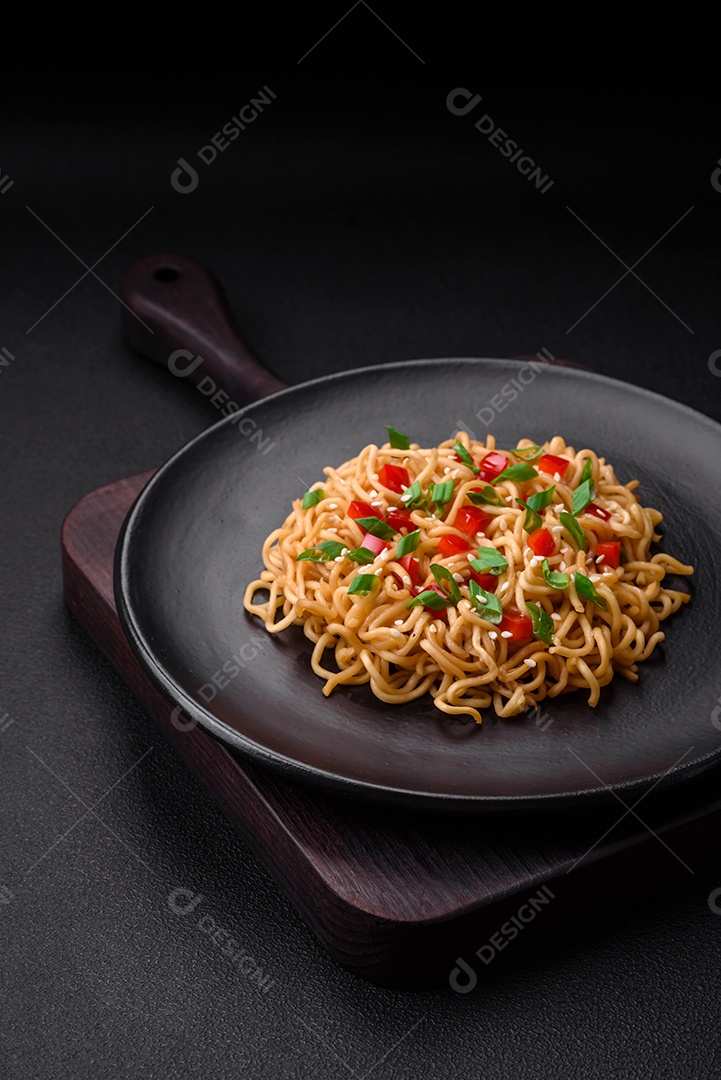 Delicioso macarrão asiático fresco com legumes, sal, especiarias e ervas em uma placa cerâmica sobre um fundo escuro de concreto