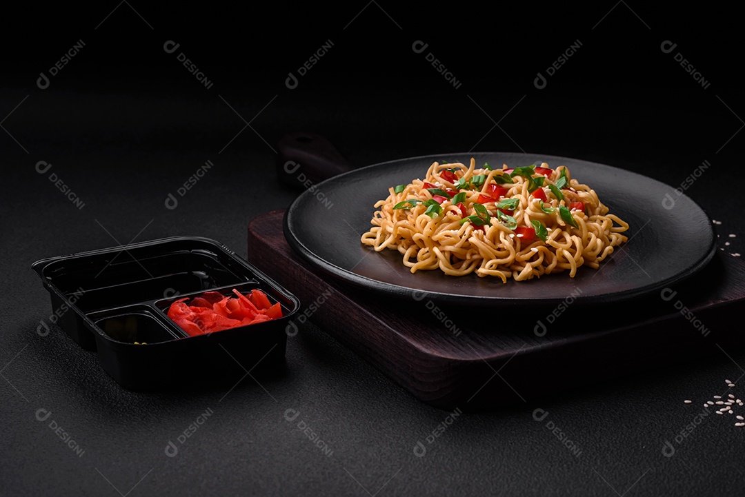 Delicioso macarrão asiático fresco com legumes, sal, especiarias e ervas em uma placa cerâmica sobre um fundo escuro de concreto