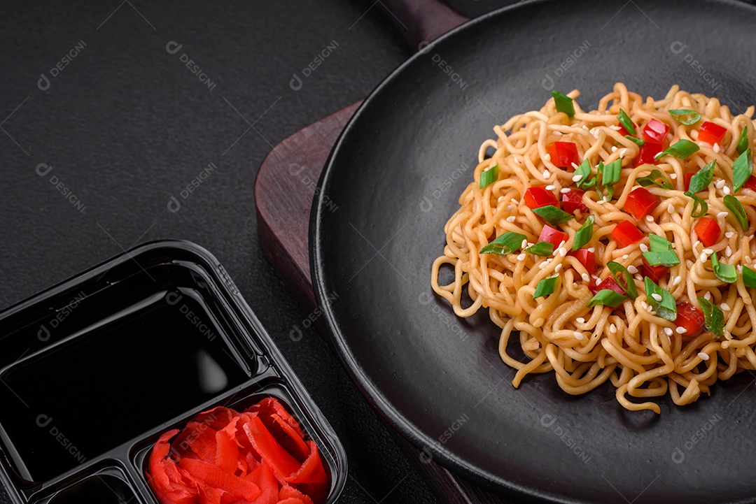 Delicioso macarrão asiático fresco com legumes, sal, especiarias e ervas em uma placa cerâmica sobre um fundo escuro de concreto