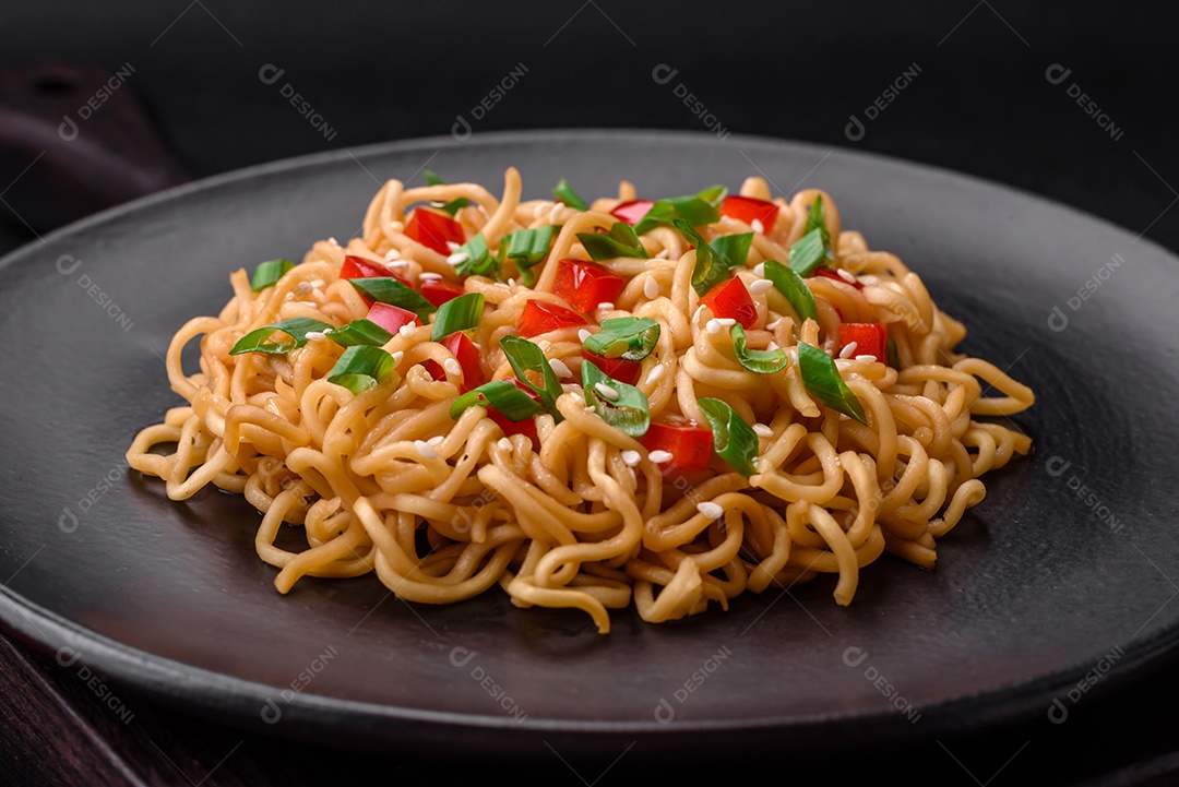 Delicioso macarrão asiático fresco com legumes, sal, especiarias e ervas em uma placa cerâmica sobre um fundo escuro de concreto