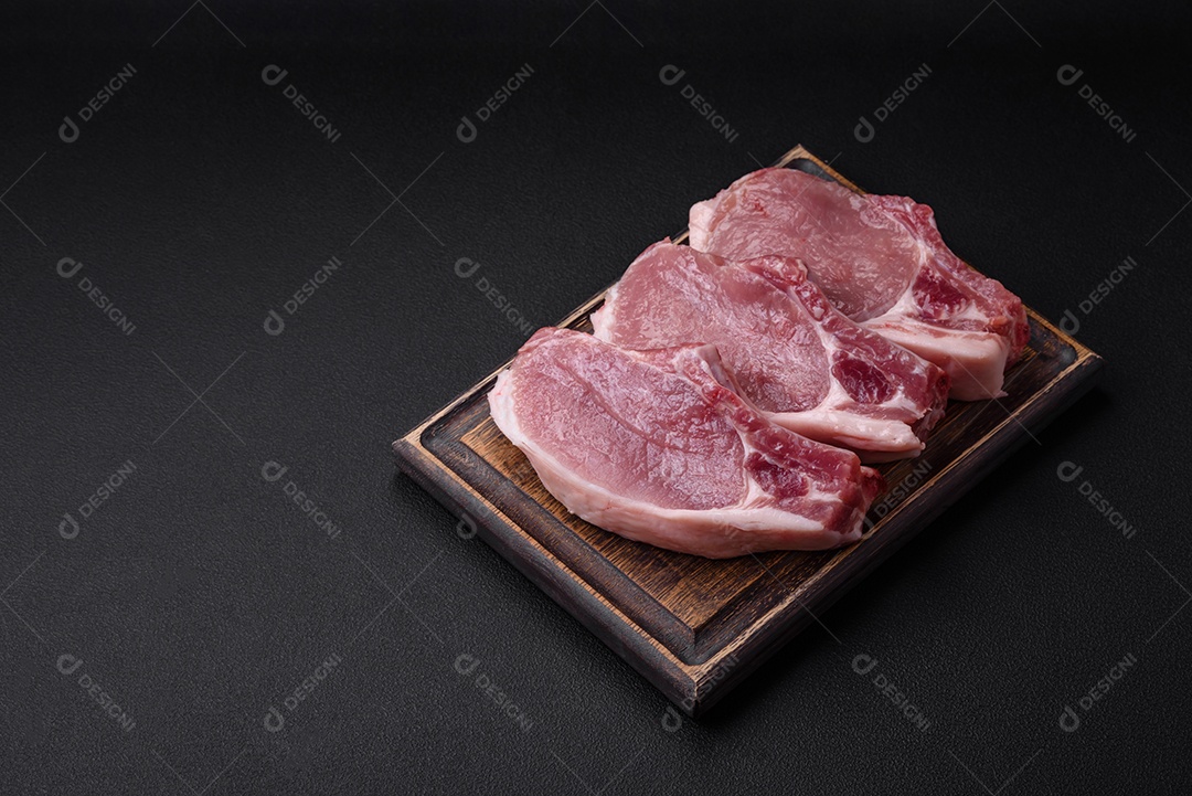 Carne de porco crua com osso ou costela cortada com sal, especiarias e ervas sobre um fundo escuro de concreto