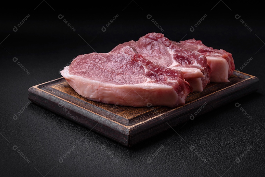 Carne de porco crua com osso ou costela cortada com sal, especiarias e ervas sobre um fundo escuro de concreto