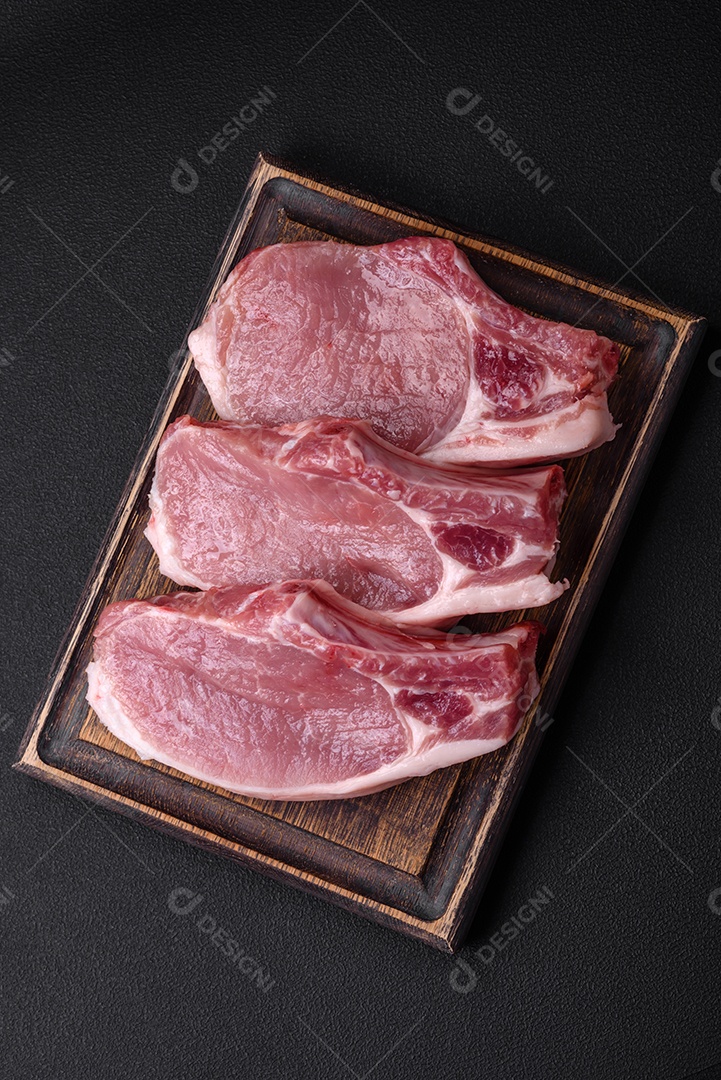Carne de porco crua com osso ou costela cortada com sal, especiarias e ervas sobre um fundo escuro de concreto