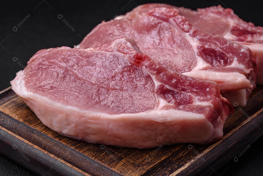 Carne de porco crua com osso ou costela cortada com sal, especiarias e ervas sobre um fundo escuro de concreto