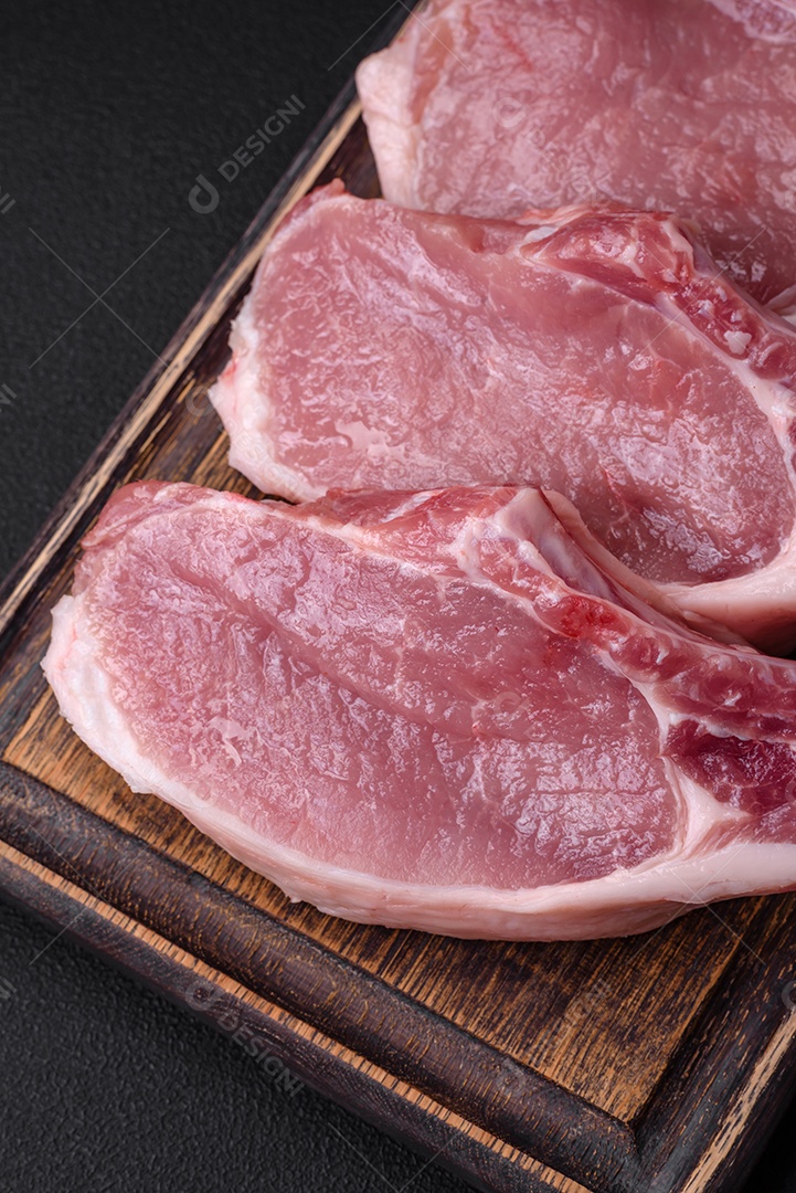 Carne de porco crua com osso ou costela cortada com sal, especiarias e ervas sobre um fundo escuro de concreto
