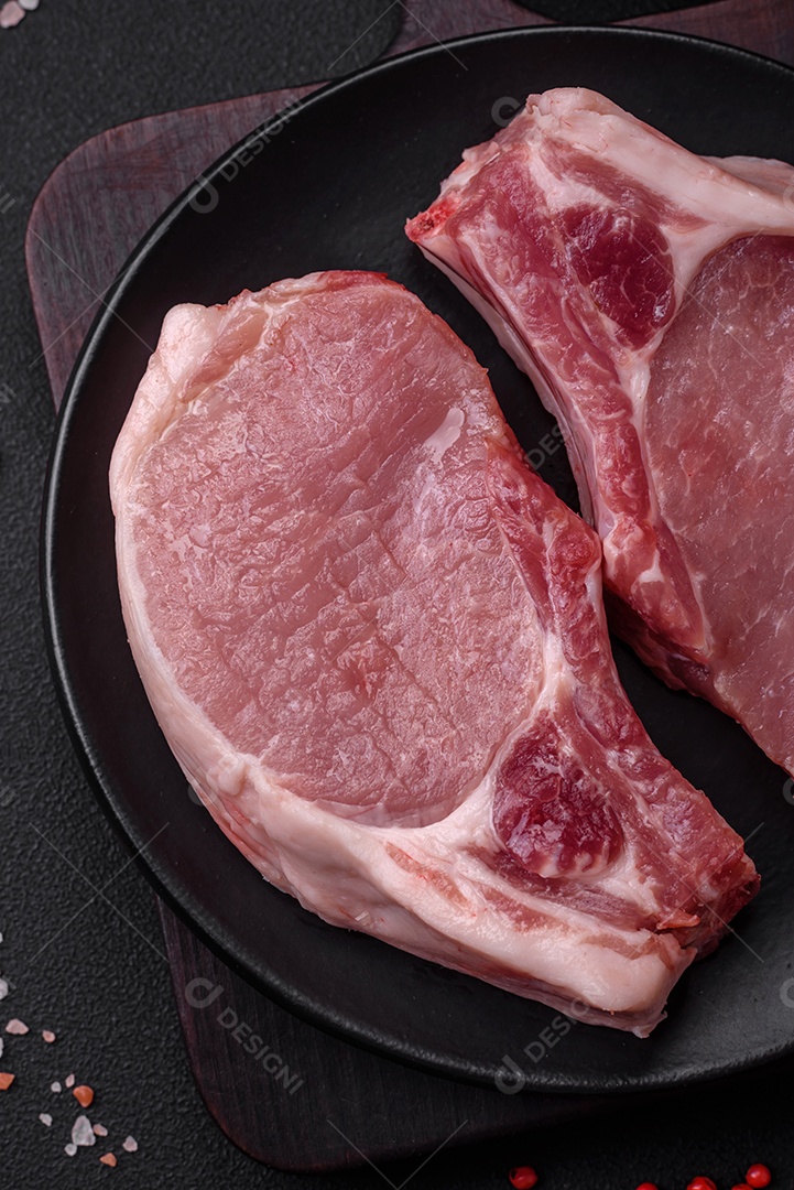 Carne de porco crua com osso ou costela cortada com sal, especiarias e ervas sobre um fundo escuro de concreto
