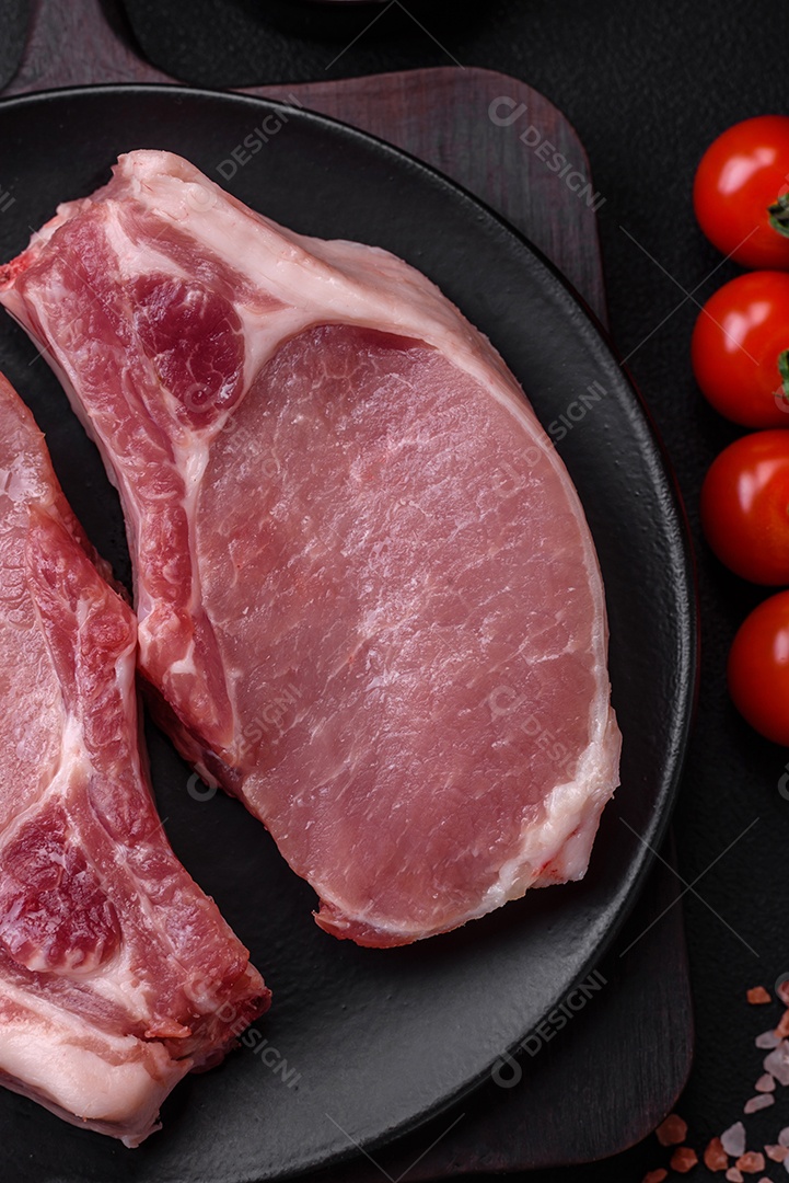 Carne de porco crua com osso ou costela cortada com sal, especiarias e ervas sobre um fundo escuro de concreto