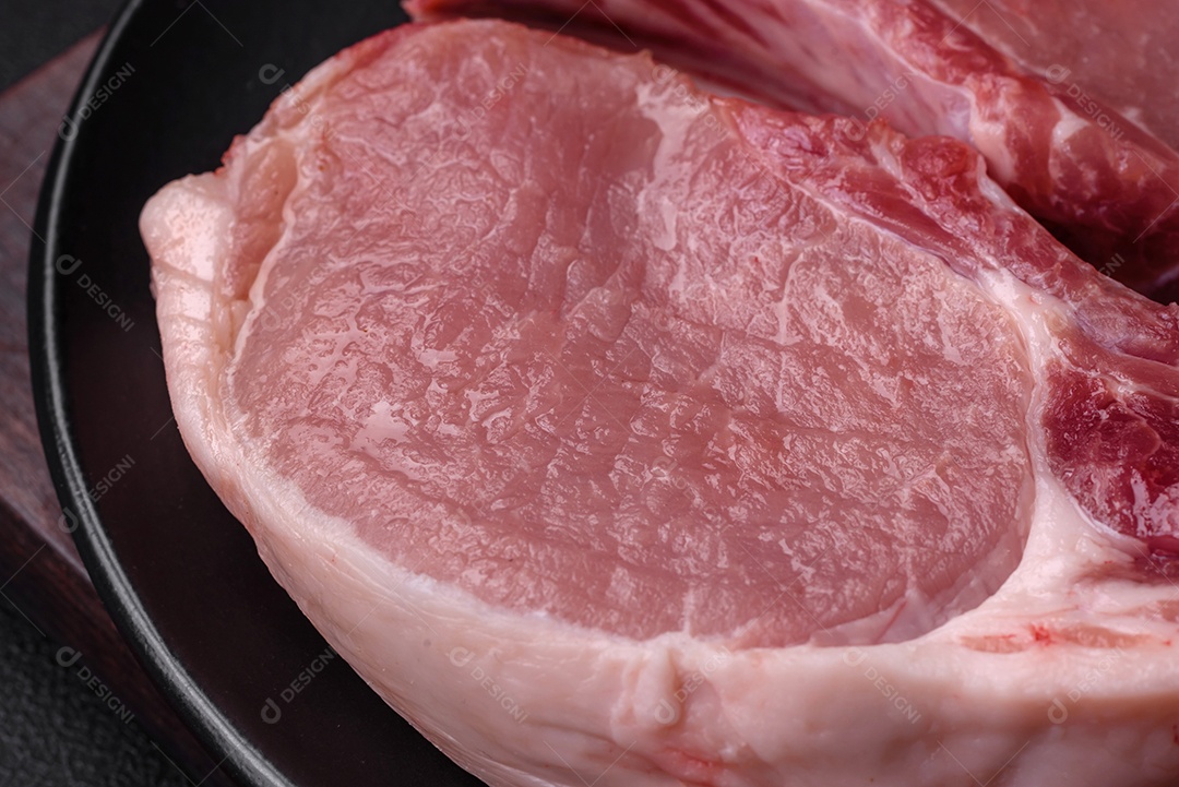 Carne de porco crua com osso ou costela cortada com sal, especiarias e ervas sobre um fundo escuro de concreto