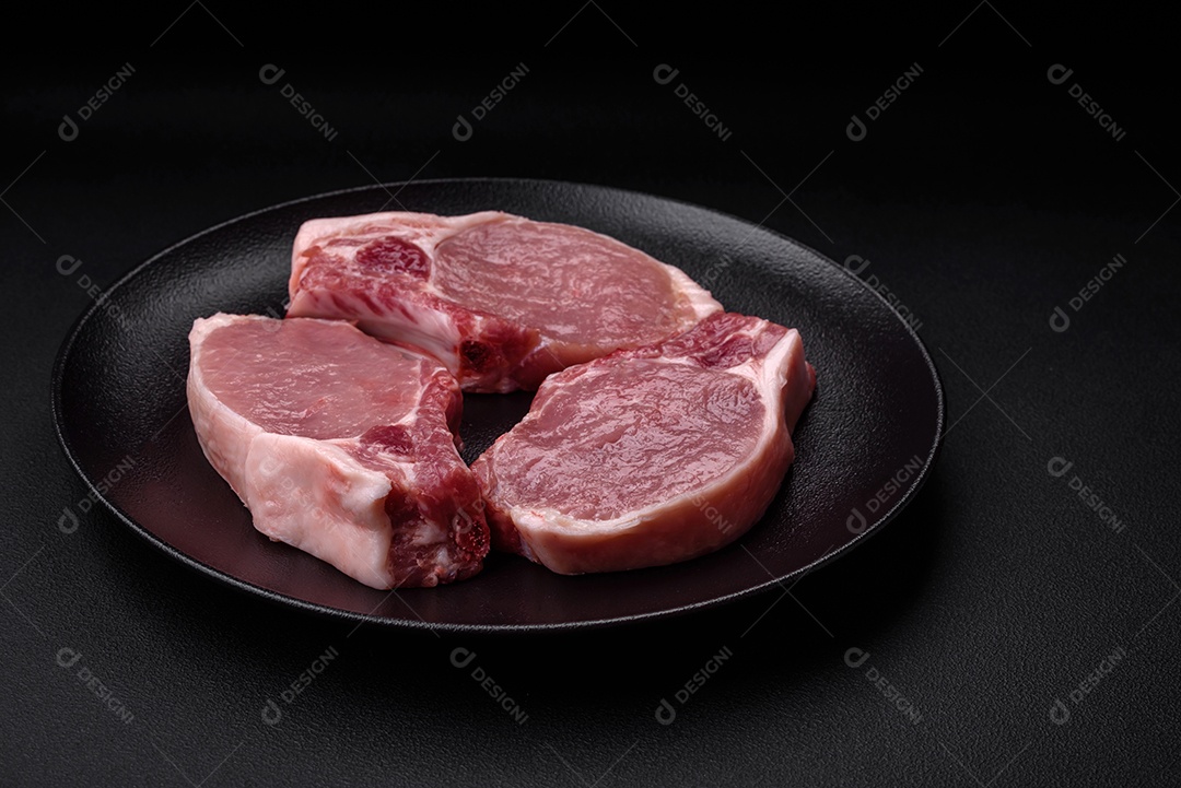 Carne de porco crua com osso ou costela cortada com sal, especiarias e ervas sobre um fundo escuro de concreto