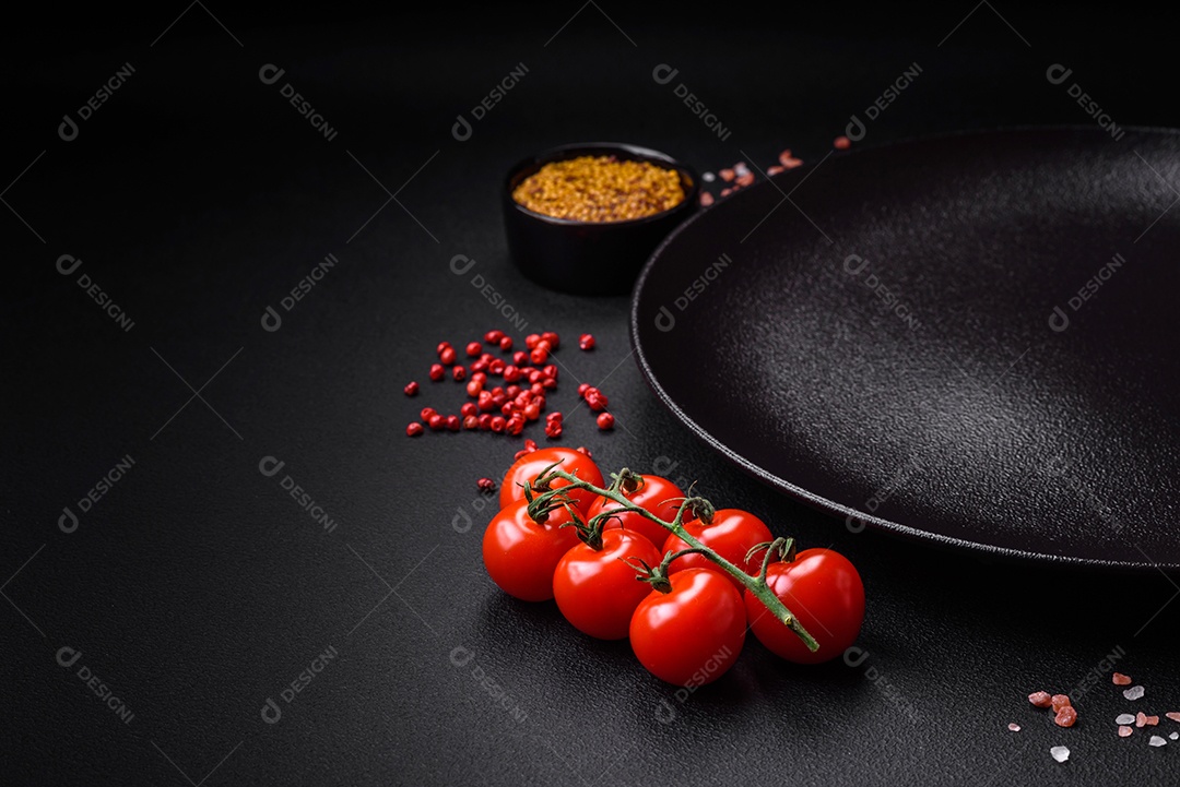 Mesa vazia de textura preta, tomate cereja em um galho, especiarias, sal e ervas. Ingredientes para cozinhar em casa