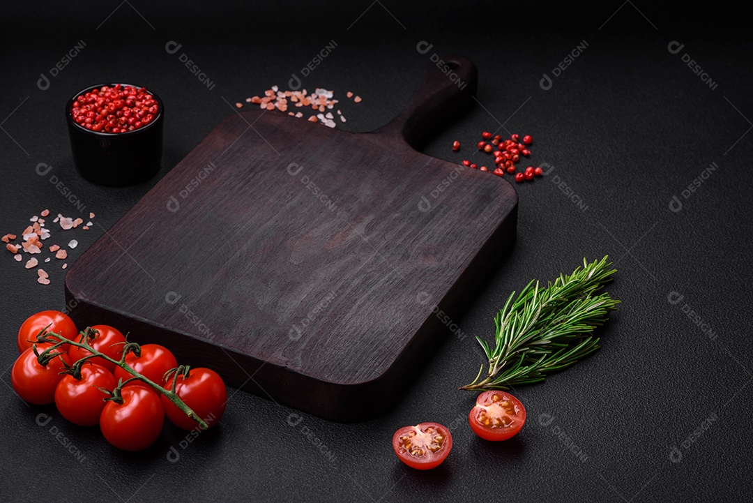 Deliciosos tomates cereja frescos em um galho com especiarias e ervas sobre um fundo escuro de concreto