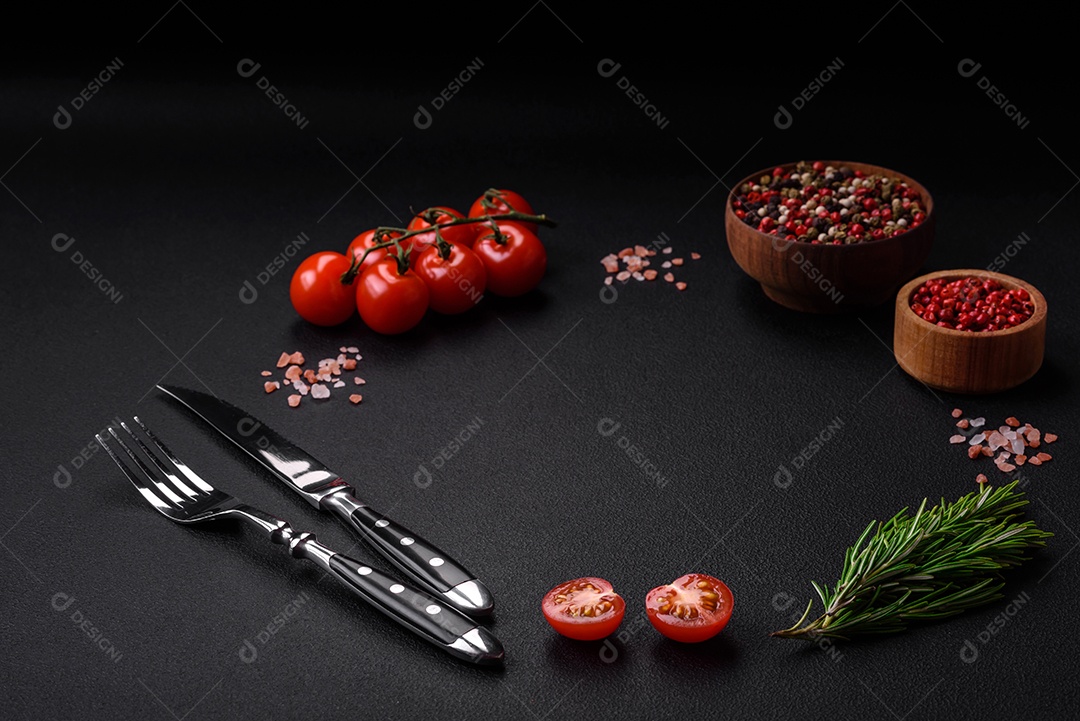 Deliciosos tomates cereja frescos em um galho com especiarias e ervas sobre um fundo escuro de concreto