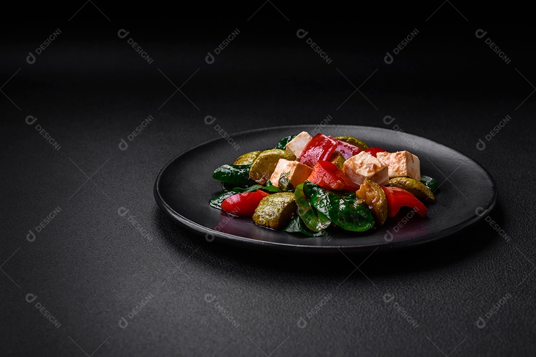 Deliciosa salada fresca de abobrinha, queijo, pimentão, espinafre com especiarias e ervas em um prato de cerâmica sobre um fundo escuro de concreto