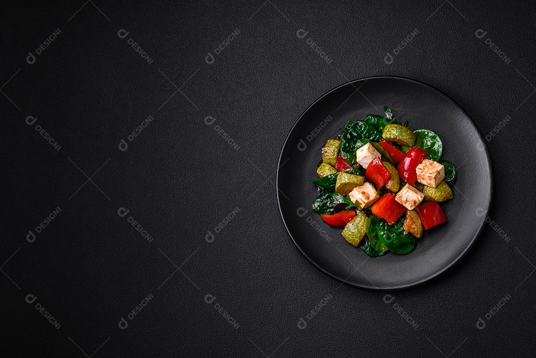 Deliciosa salada fresca de abobrinha, queijo, pimentão, espinafre com especiarias e ervas em um prato de cerâmica sobre um fundo escuro de concreto