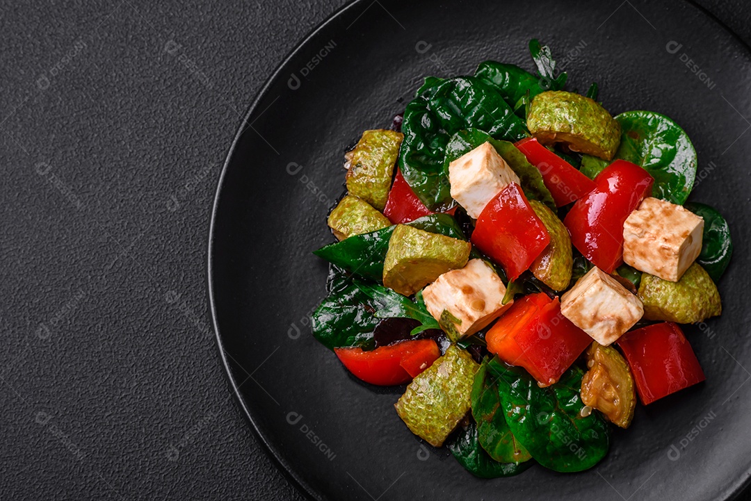 Deliciosa salada fresca de abobrinha, queijo, pimentão, espinafre com especiarias e ervas em um prato de cerâmica sobre um fundo escuro de concreto