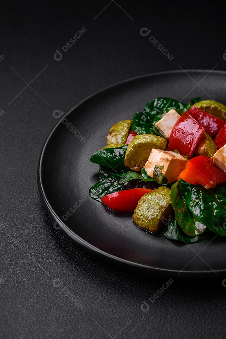 Deliciosa salada fresca de abobrinha, queijo, pimentão, espinafre com especiarias e ervas em um prato de cerâmica sobre um fundo escuro de concreto