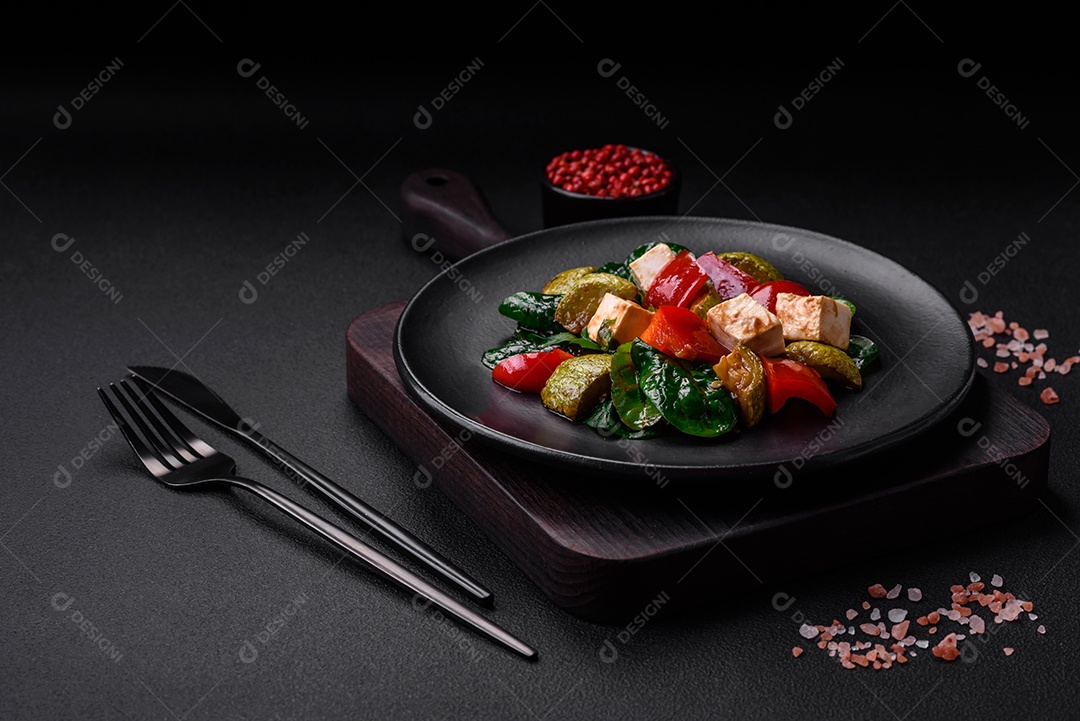 Deliciosa salada fresca de abobrinha, queijo, pimentão, espinafre com especiarias e ervas em um prato de cerâmica sobre um fundo escuro de concreto