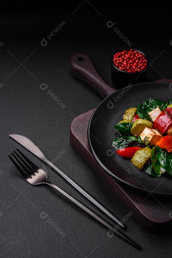 Deliciosa salada fresca de abobrinha, queijo, pimentão, espinafre com especiarias e ervas em um prato de cerâmica sobre um fundo escuro de concreto