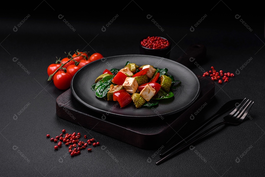 Deliciosa salada fresca de abobrinha, queijo, pimentão, espinafre com especiarias e ervas em um prato de cerâmica sobre um fundo escuro de concreto