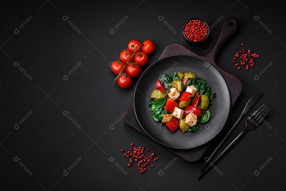 Deliciosa salada fresca de abobrinha, queijo, pimentão, espinafre com especiarias e ervas em um prato de cerâmica sobre um fundo escuro de concreto