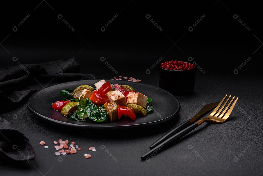 Deliciosa salada fresca de abobrinha, queijo, pimentão, espinafre com especiarias e ervas em um prato de cerâmica sobre um fundo escuro de concreto