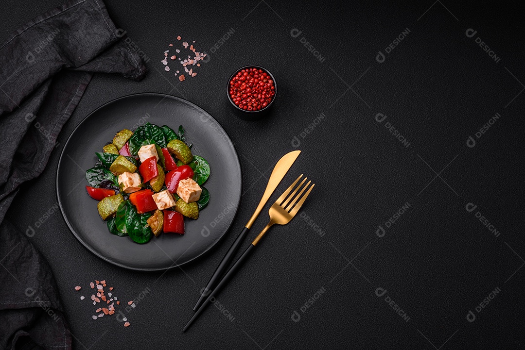 Deliciosa salada fresca de abobrinha, queijo, pimentão, espinafre com especiarias e ervas em um prato de cerâmica sobre um fundo escuro de concreto