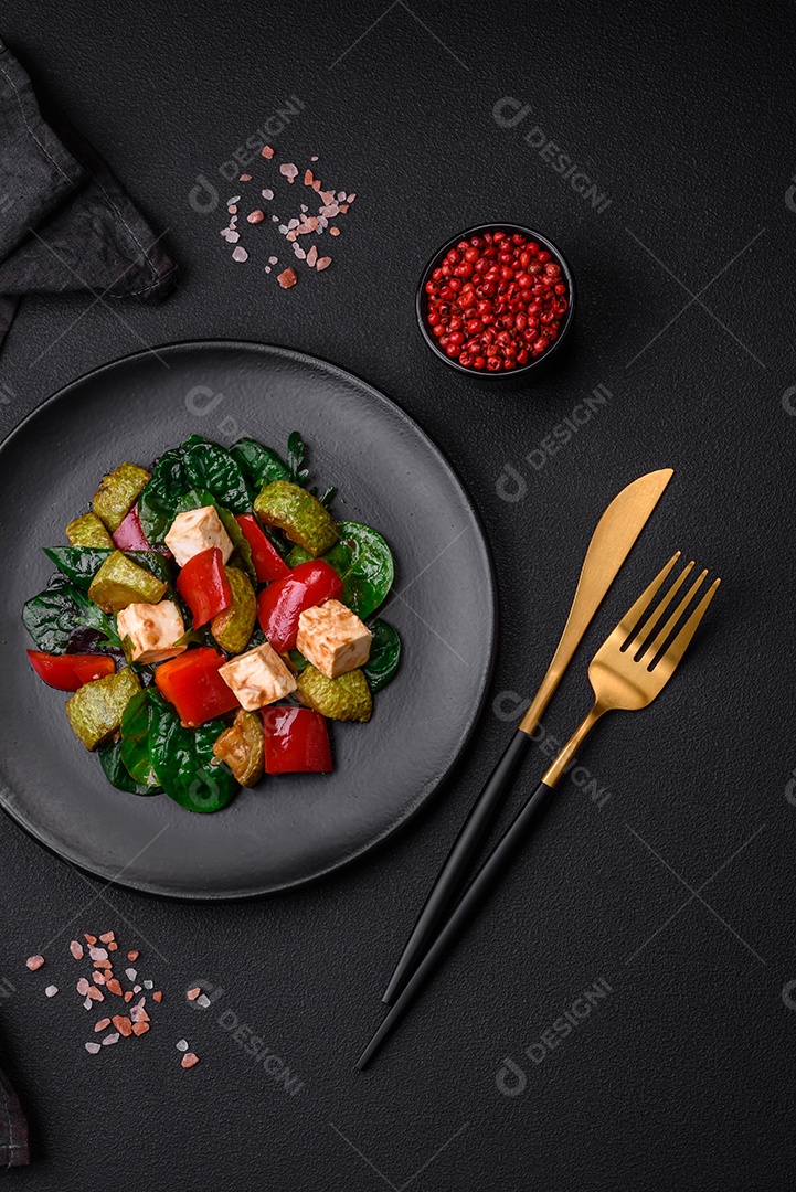 Deliciosa salada fresca de abobrinha, queijo, pimentão, espinafre com especiarias e ervas em um prato de cerâmica sobre um fundo escuro de concreto