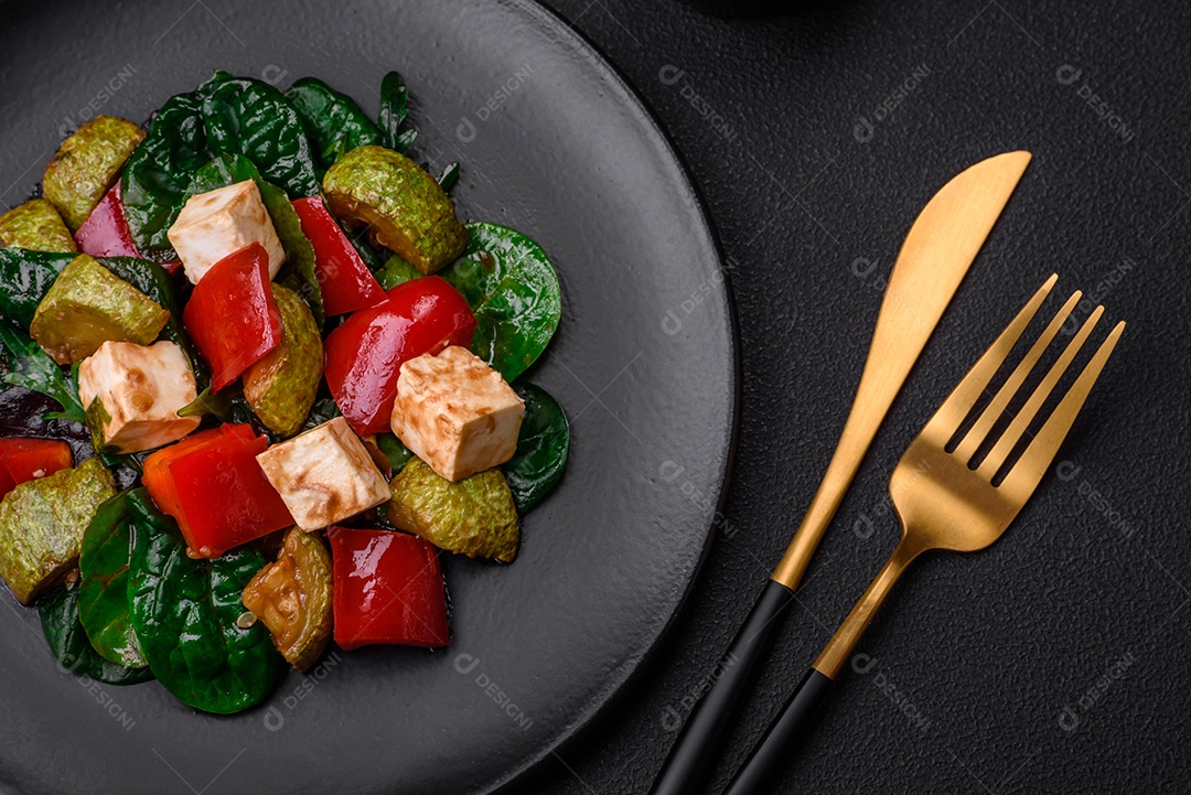 Deliciosa salada fresca de abobrinha, queijo, pimentão, espinafre com especiarias e ervas em um prato de cerâmica sobre um fundo escuro de concreto