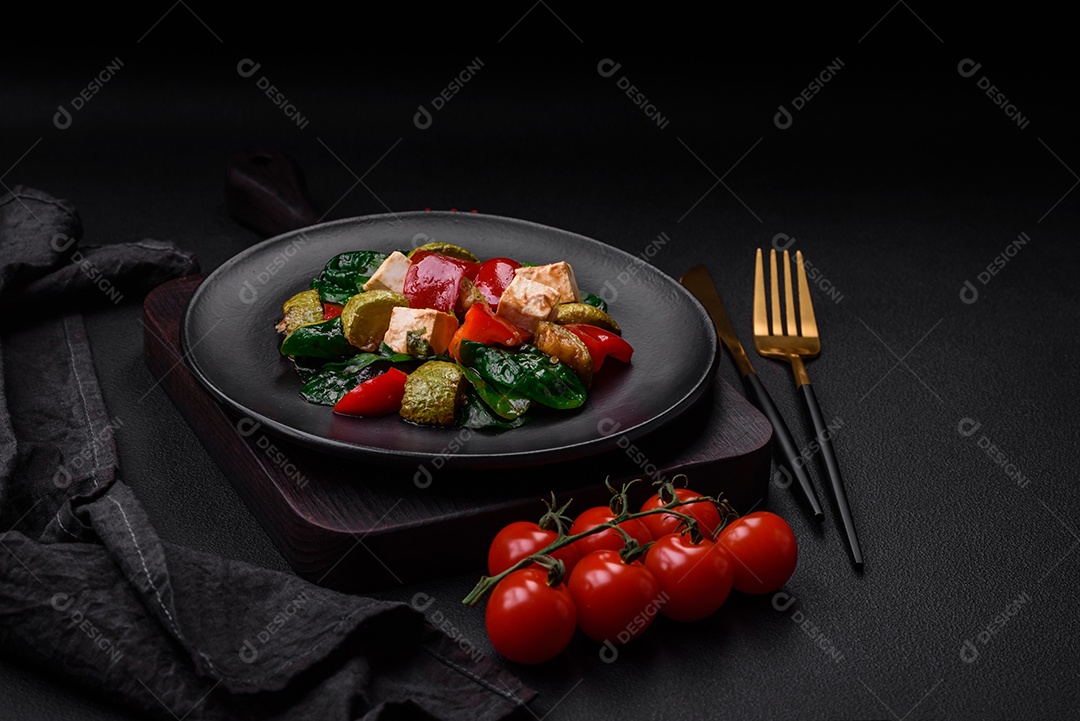 Deliciosa salada fresca de abobrinha, queijo, pimentão, espinafre com especiarias e ervas em um prato de cerâmica sobre um fundo escuro de concreto