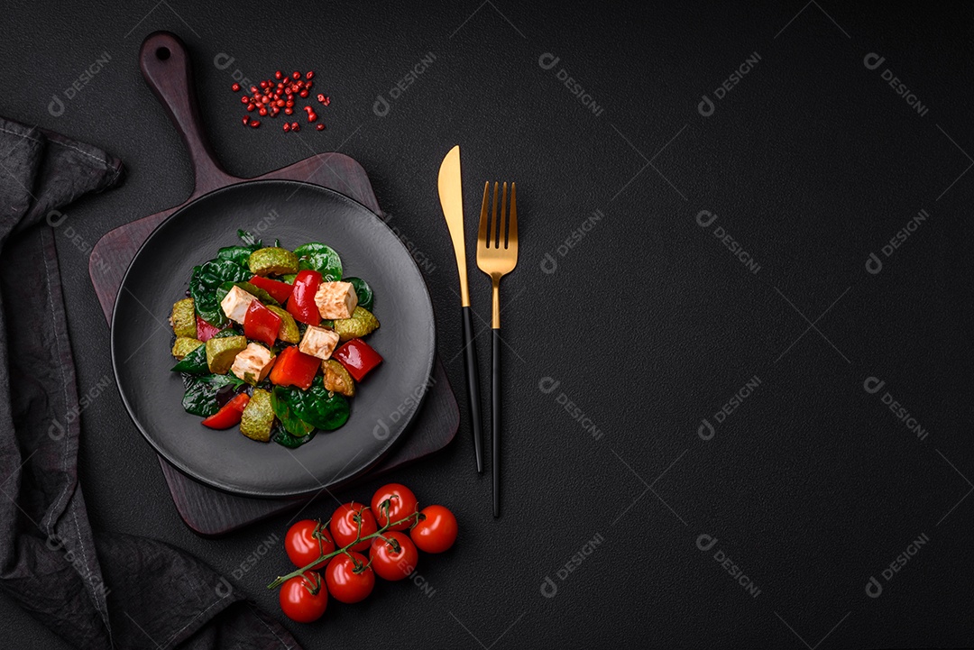 Deliciosa salada fresca de abobrinha, queijo, pimentão, espinafre com especiarias e ervas em um prato de cerâmica sobre um fundo escuro de concreto