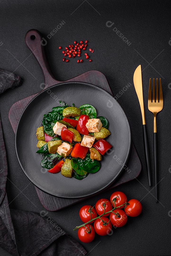Deliciosa salada fresca de abobrinha, queijo, pimentão, espinafre com especiarias e ervas em um prato de cerâmica sobre um fundo escuro de concreto