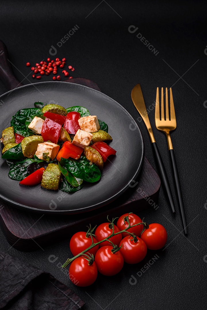 Deliciosa salada fresca de abobrinha, queijo, pimentão, espinafre com especiarias e ervas em um prato de cerâmica sobre um fundo escuro de concreto