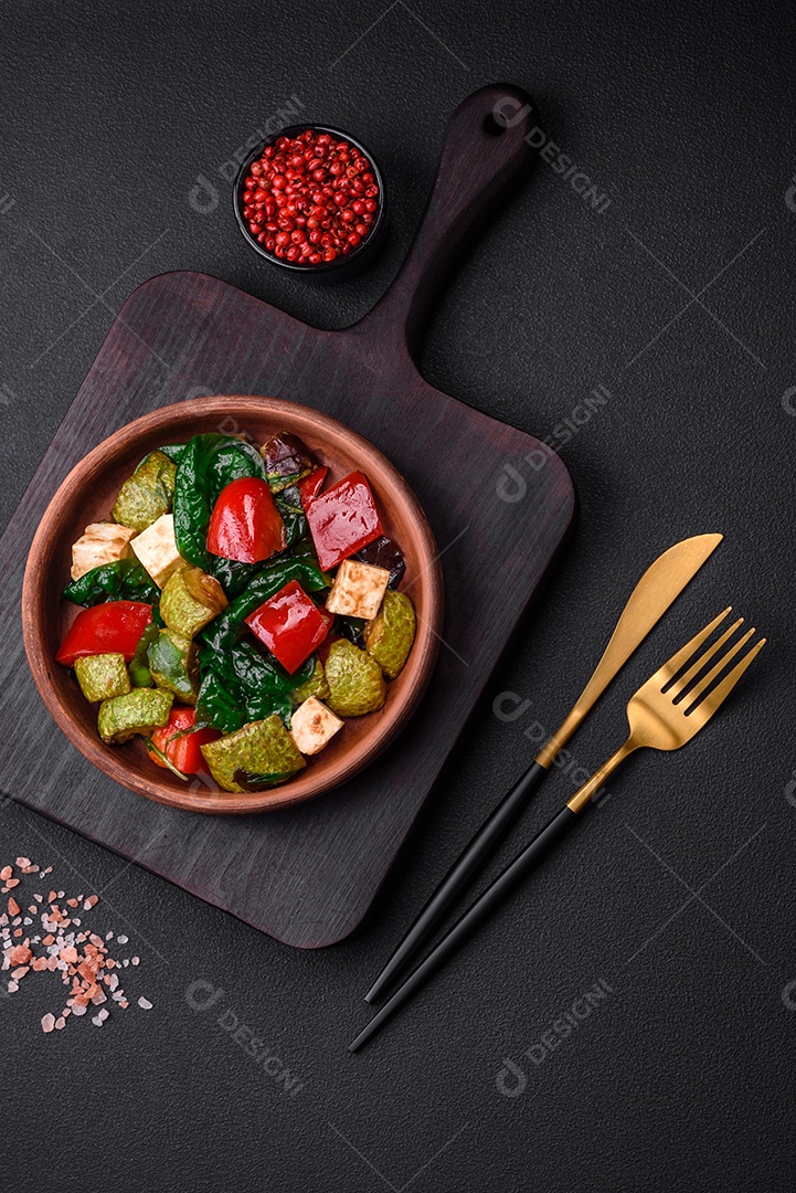 Deliciosa salada fresca de abobrinha, queijo, pimentão, espinafre com especiarias e ervas em um prato de cerâmica sobre um fundo escuro de concreto