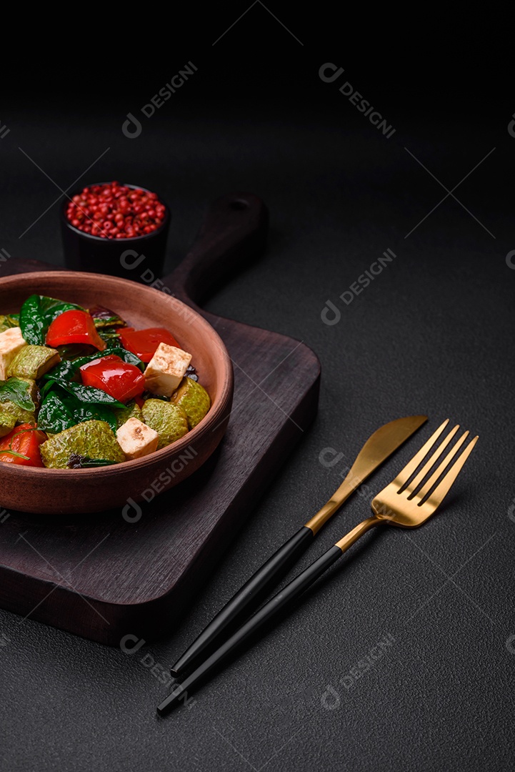 Deliciosa salada fresca de abobrinha, queijo, pimentão, espinafre com especiarias e ervas em um prato de cerâmica sobre um fundo escuro de concreto