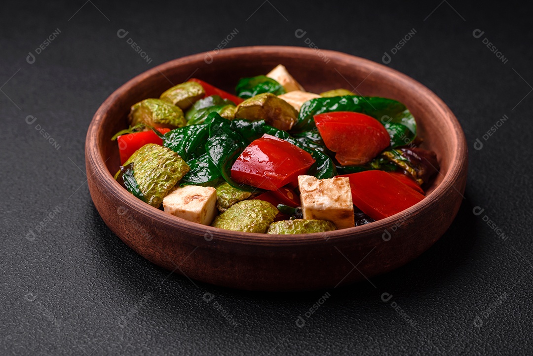 Deliciosa salada fresca de abobrinha, queijo, pimentão, espinafre com especiarias e ervas em um prato de cerâmica sobre um fundo escuro de concreto