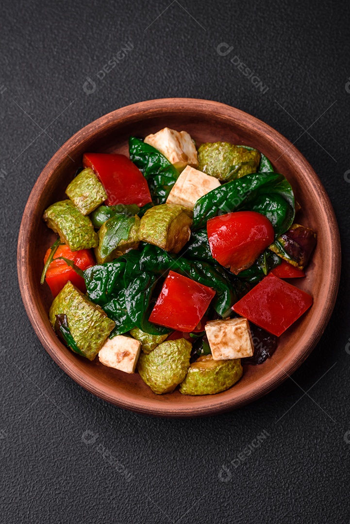 Deliciosa salada fresca de abobrinha, queijo, pimentão, espinafre com especiarias e ervas em um prato de cerâmica sobre um fundo escuro de concreto