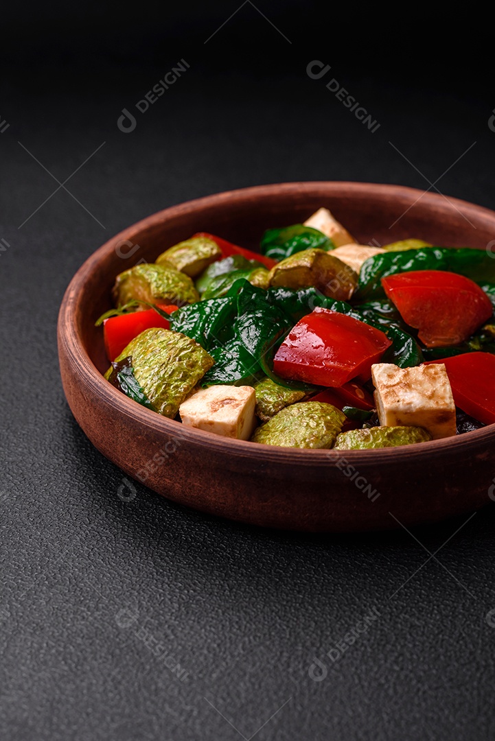 Deliciosa salada fresca de abobrinha, queijo, pimentão, espinafre com especiarias e ervas em um prato de cerâmica sobre um fundo escuro de concreto